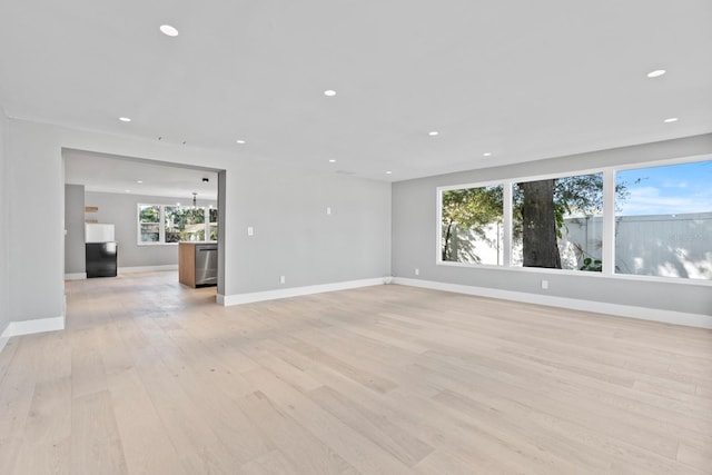 unfurnished living room with recessed lighting, a notable chandelier, light wood-style flooring, and baseboards