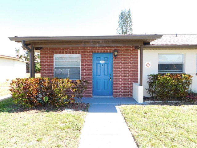 doorway to property featuring brick siding and a yard