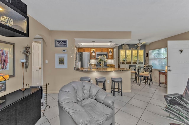 living area featuring arched walkways, ceiling fan, baseboards, and light tile patterned floors