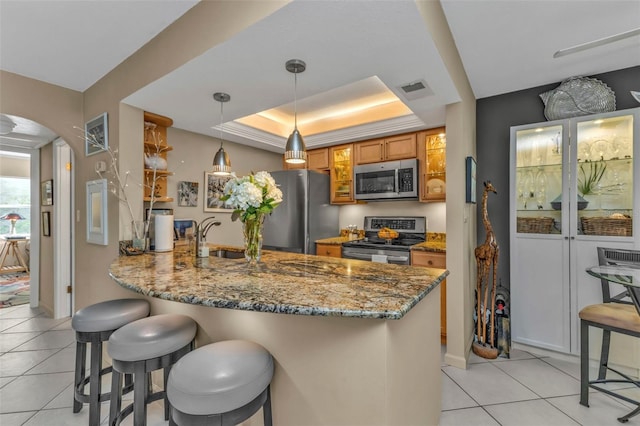 kitchen with arched walkways, a raised ceiling, appliances with stainless steel finishes, a sink, and a peninsula