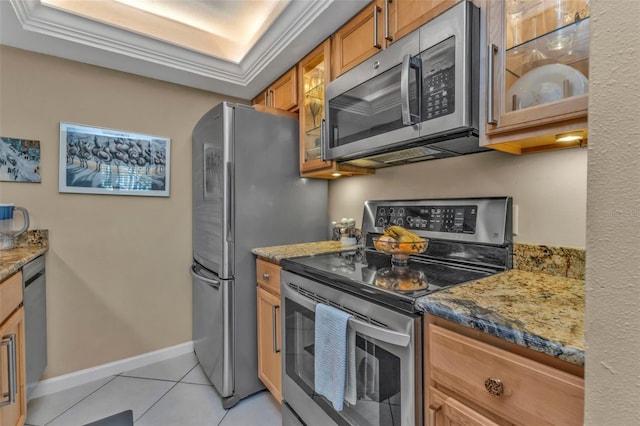 kitchen featuring light tile patterned floors, baseboards, brown cabinetry, glass insert cabinets, and stainless steel appliances