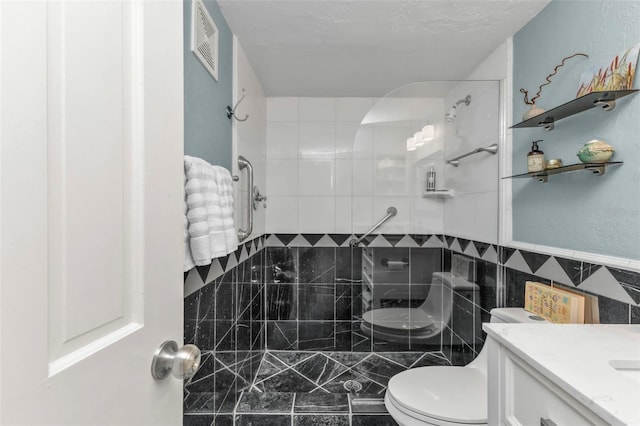 bathroom featuring toilet, tiled shower, vanity, and tile walls