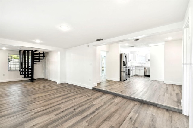 unfurnished living room featuring a sink, visible vents, baseboards, stairs, and light wood finished floors