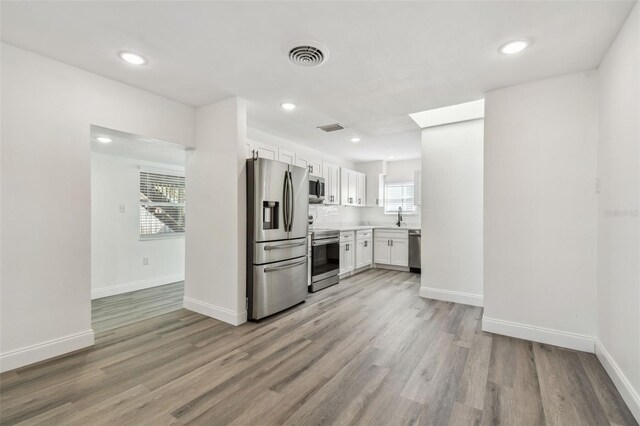 kitchen with light wood finished floors, appliances with stainless steel finishes, visible vents, and white cabinets