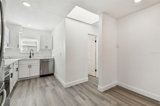 kitchen featuring dishwasher, light countertops, a sink, and baseboards