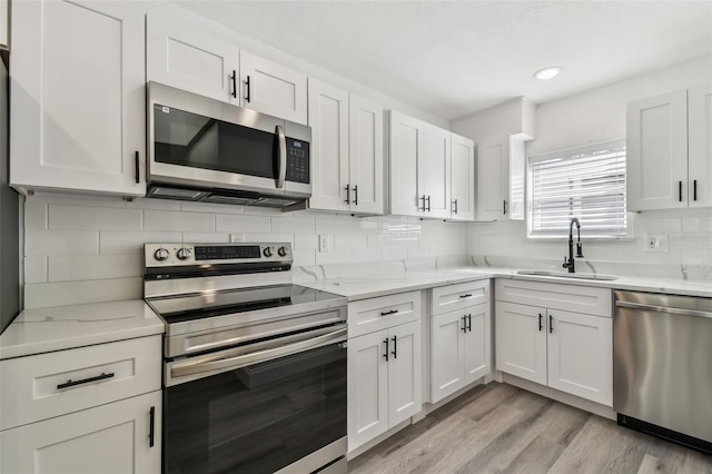 kitchen featuring stainless steel appliances, a sink, white cabinets, light wood-type flooring, and tasteful backsplash