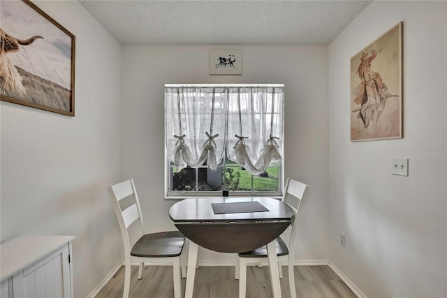 dining area featuring a textured ceiling, light wood-type flooring, and baseboards