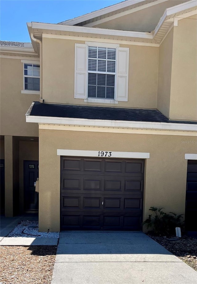 view of front facade featuring concrete driveway, roof with shingles, an attached garage, and stucco siding