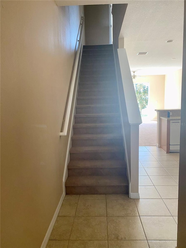 stairs with a textured ceiling, baseboards, and tile patterned floors