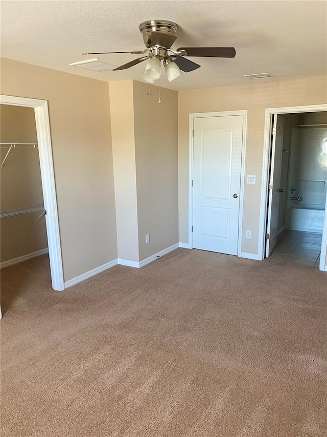 unfurnished bedroom featuring baseboards, carpet, a walk in closet, a textured ceiling, and a closet