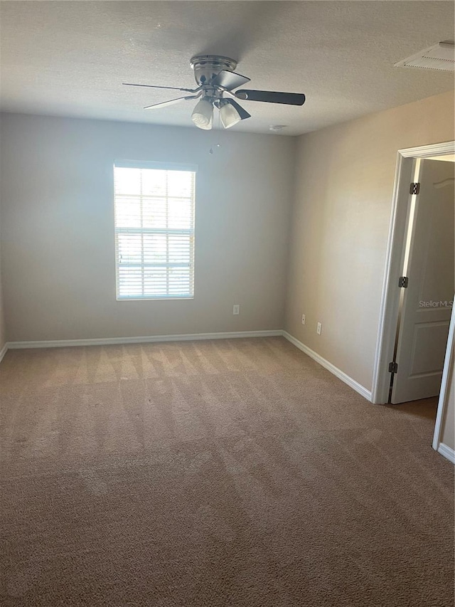 empty room with light carpet, a ceiling fan, baseboards, and a textured ceiling