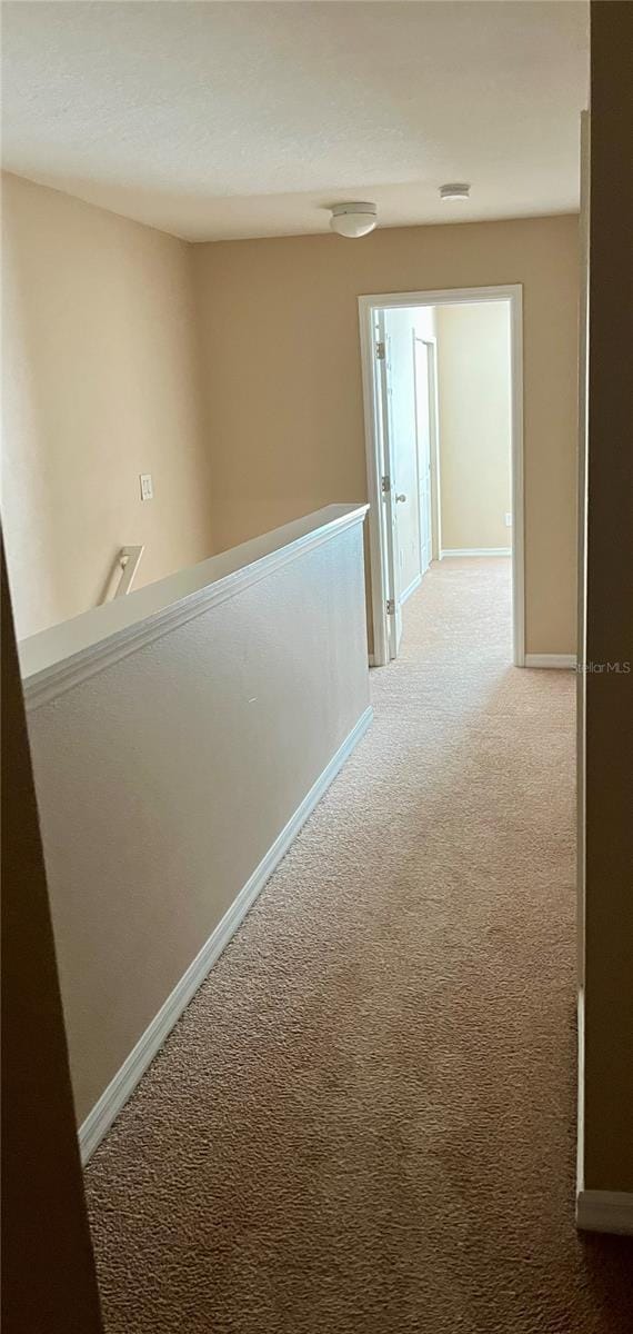 hall with baseboards, an upstairs landing, and light colored carpet