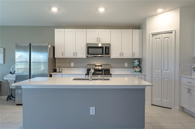 kitchen featuring a kitchen island with sink, stainless steel appliances, a sink, white cabinets, and light countertops