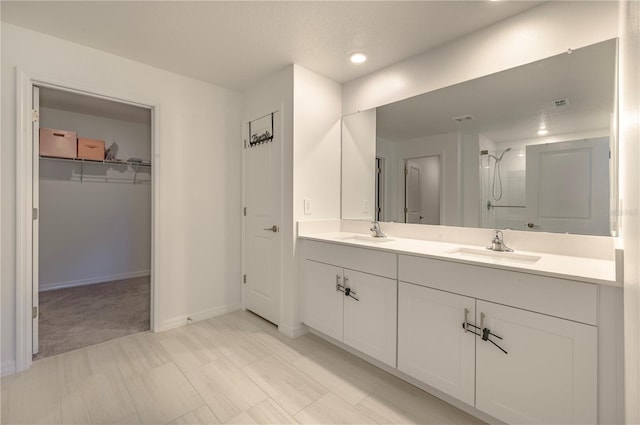 full bathroom with a walk in closet, double vanity, walk in shower, and a sink