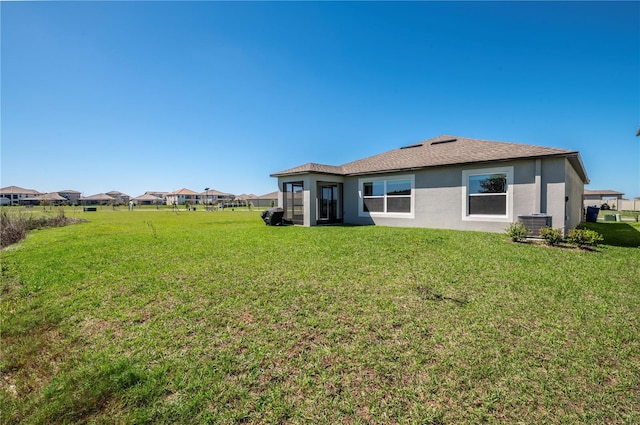 rear view of property with central air condition unit, a lawn, and stucco siding