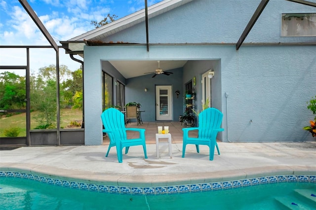 rear view of house with glass enclosure, a patio area, a ceiling fan, and stucco siding