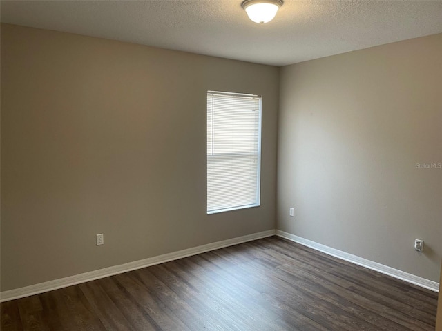 spare room featuring dark wood-type flooring, a textured ceiling, and baseboards