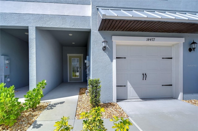 entrance to property with metal roof, concrete driveway, a standing seam roof, and stucco siding