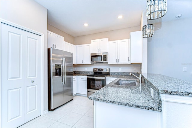 kitchen featuring a peninsula, a sink, white cabinetry, appliances with stainless steel finishes, and light stone countertops