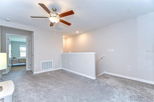 carpeted empty room with baseboards, visible vents, and a ceiling fan