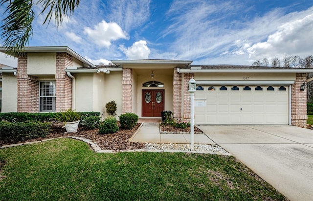 view of front of house featuring an attached garage, brick siding, driveway, stucco siding, and a front lawn