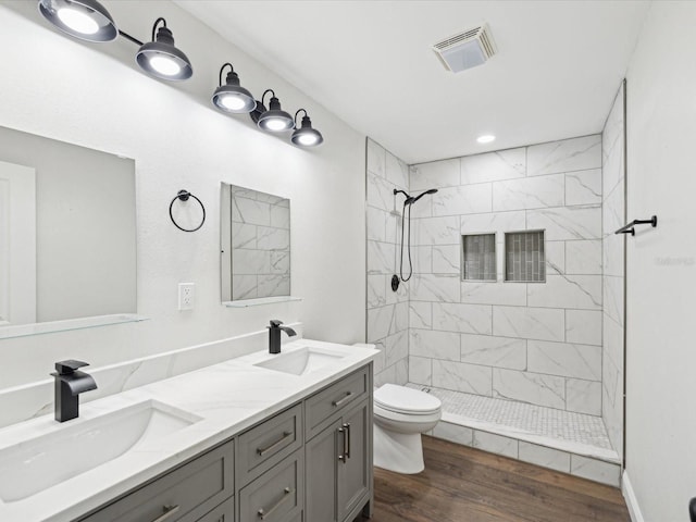 full bathroom with visible vents, tiled shower, toilet, and a sink