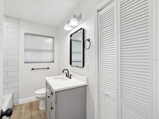 full bath featuring baseboards, toilet, wood finished floors, a closet, and vanity