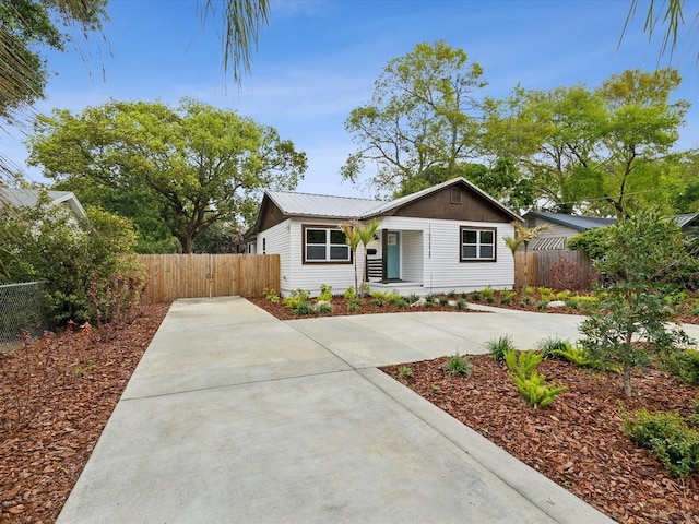 view of front facade with concrete driveway, a gate, fence, and metal roof