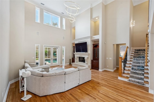 living room featuring crown molding, a notable chandelier, a fireplace, light wood-type flooring, and stairs