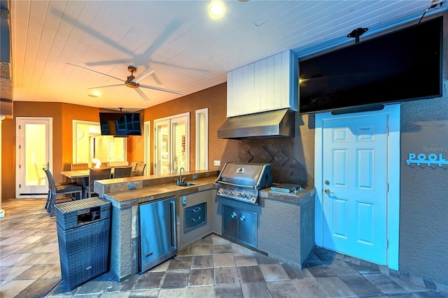 kitchen featuring refrigerator, a peninsula, stone finish flooring, under cabinet range hood, and a sink