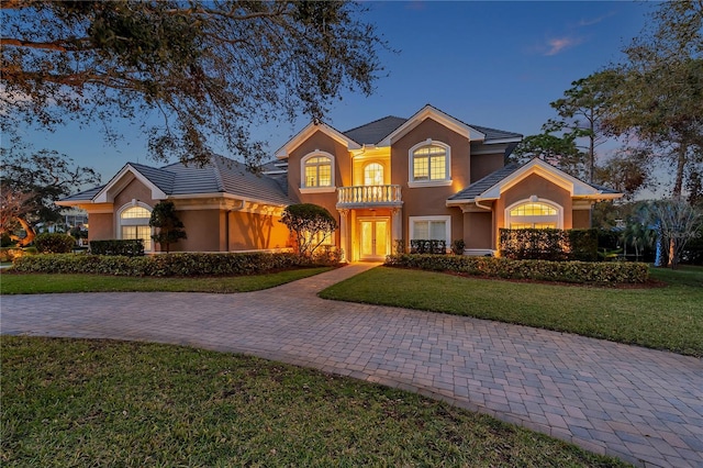 view of front of property with a tile roof, a balcony, a front lawn, and stucco siding