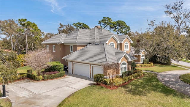 view of front facade with concrete driveway, a tile roof, a chimney, an attached garage, and a front lawn