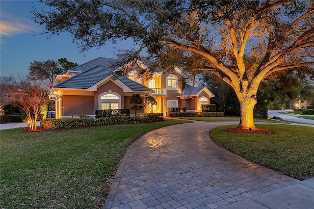 view of front of property featuring curved driveway, a tiled roof, a front lawn, and stucco siding