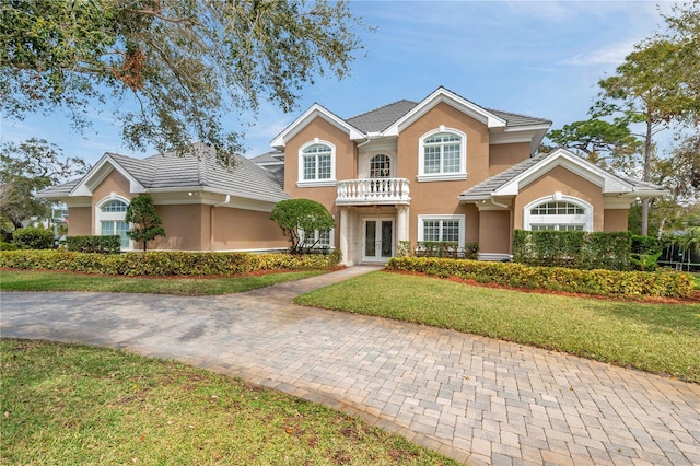 view of front of house with a balcony, a tiled roof, french doors, a front yard, and stucco siding