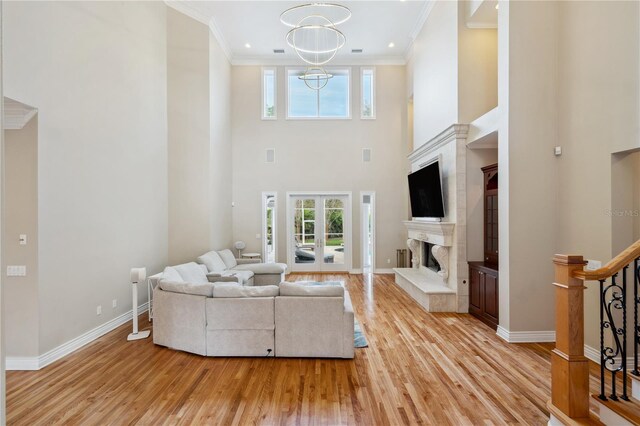 living area with a fireplace with raised hearth, baseboards, stairs, light wood-style floors, and ornamental molding