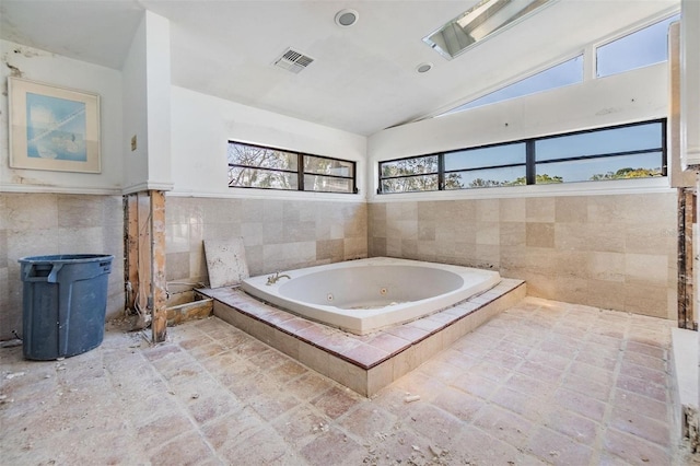 full bath with visible vents, vaulted ceiling, tile walls, and a whirlpool tub