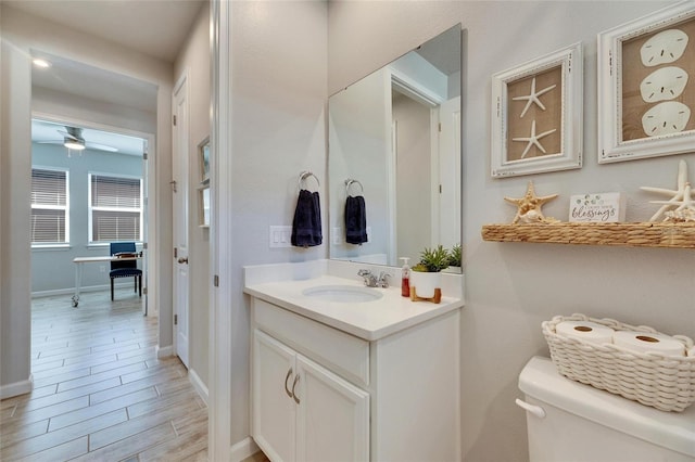 half bathroom with wood finish floors, toilet, ceiling fan, vanity, and baseboards