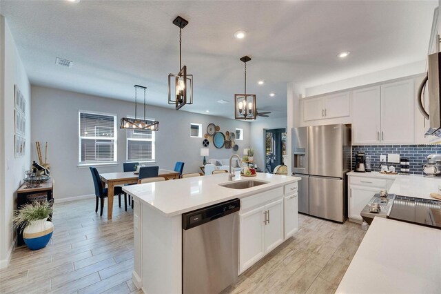 kitchen with a sink, light countertops, appliances with stainless steel finishes, tasteful backsplash, and an island with sink