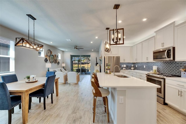 kitchen with decorative backsplash, an island with sink, stainless steel appliances, light countertops, and a sink