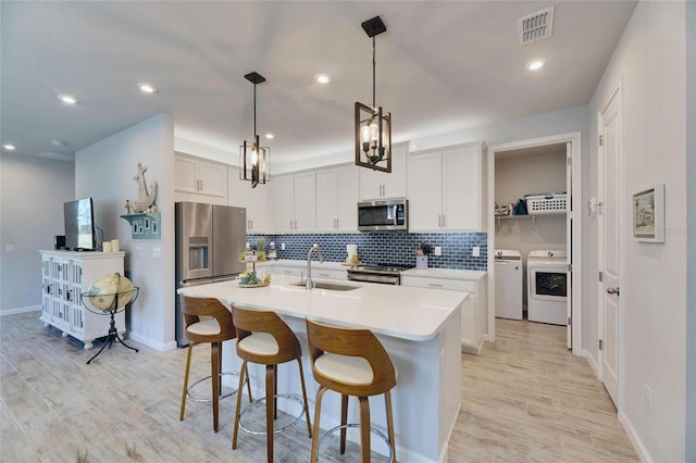 kitchen featuring stainless steel appliances, a sink, visible vents, decorative backsplash, and washer and clothes dryer