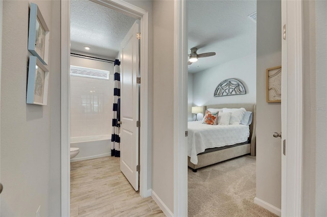 hall with baseboards, a textured ceiling, and light colored carpet