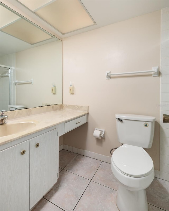 bathroom featuring a shower, toilet, vanity, baseboards, and tile patterned floors