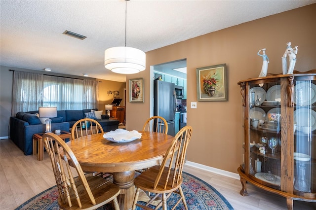 dining room featuring light wood finished floors, visible vents, a textured ceiling, and baseboards