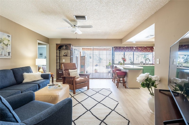 living room featuring light wood finished floors, visible vents, a textured ceiling, and ceiling fan