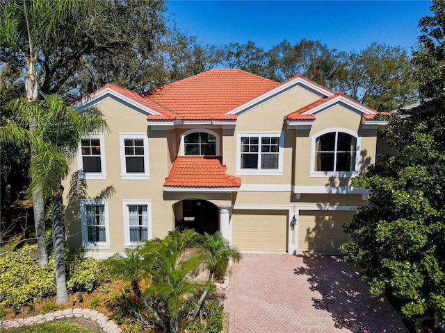 mediterranean / spanish-style home featuring a garage, decorative driveway, a tile roof, and stucco siding