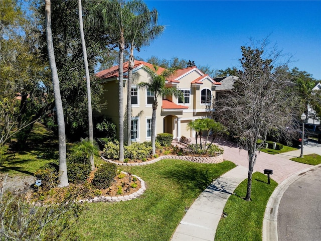 mediterranean / spanish-style house featuring a tile roof, a front lawn, and stucco siding