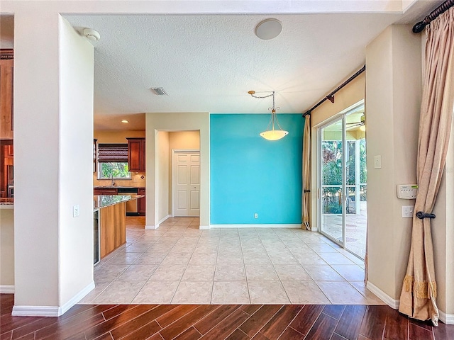 empty room featuring light wood finished floors, baseboards, visible vents, and a textured ceiling