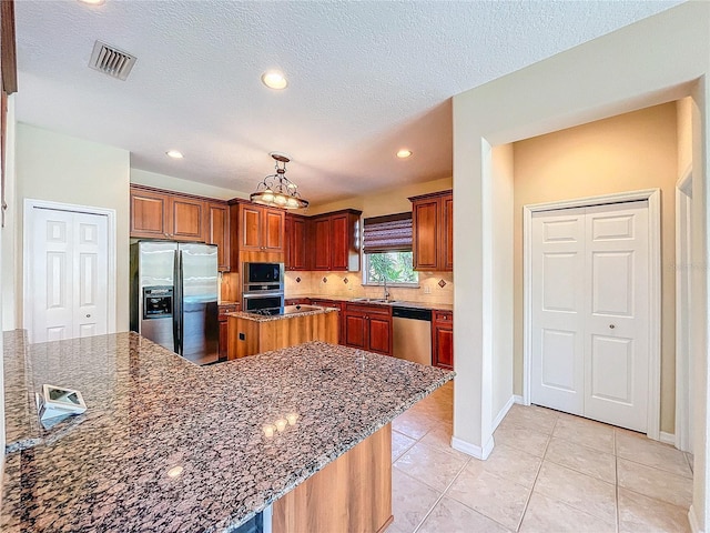 kitchen with light tile patterned floors, appliances with stainless steel finishes, dark stone countertops, a center island, and a sink