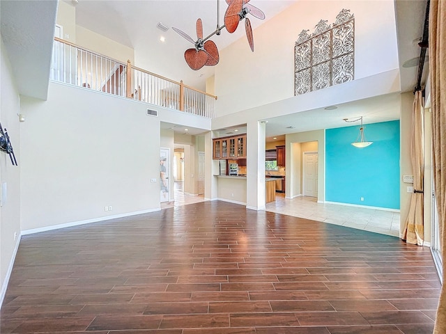 unfurnished living room with ceiling fan, wood finished floors, visible vents, and baseboards