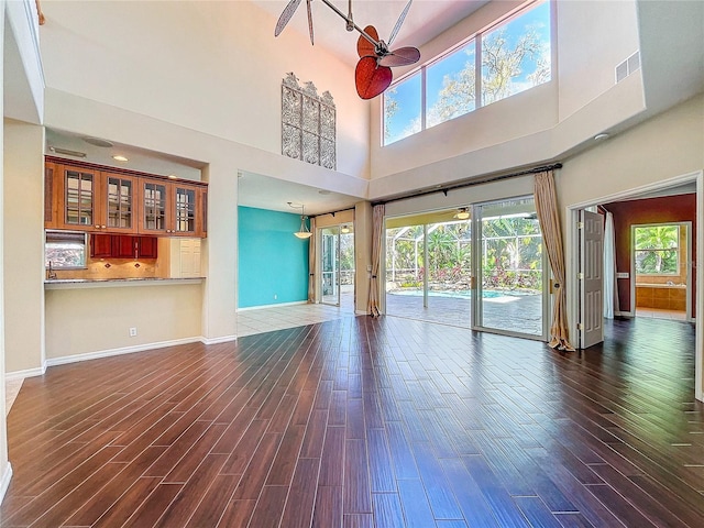 unfurnished living room featuring dark wood-style floors, visible vents, baseboards, and a ceiling fan